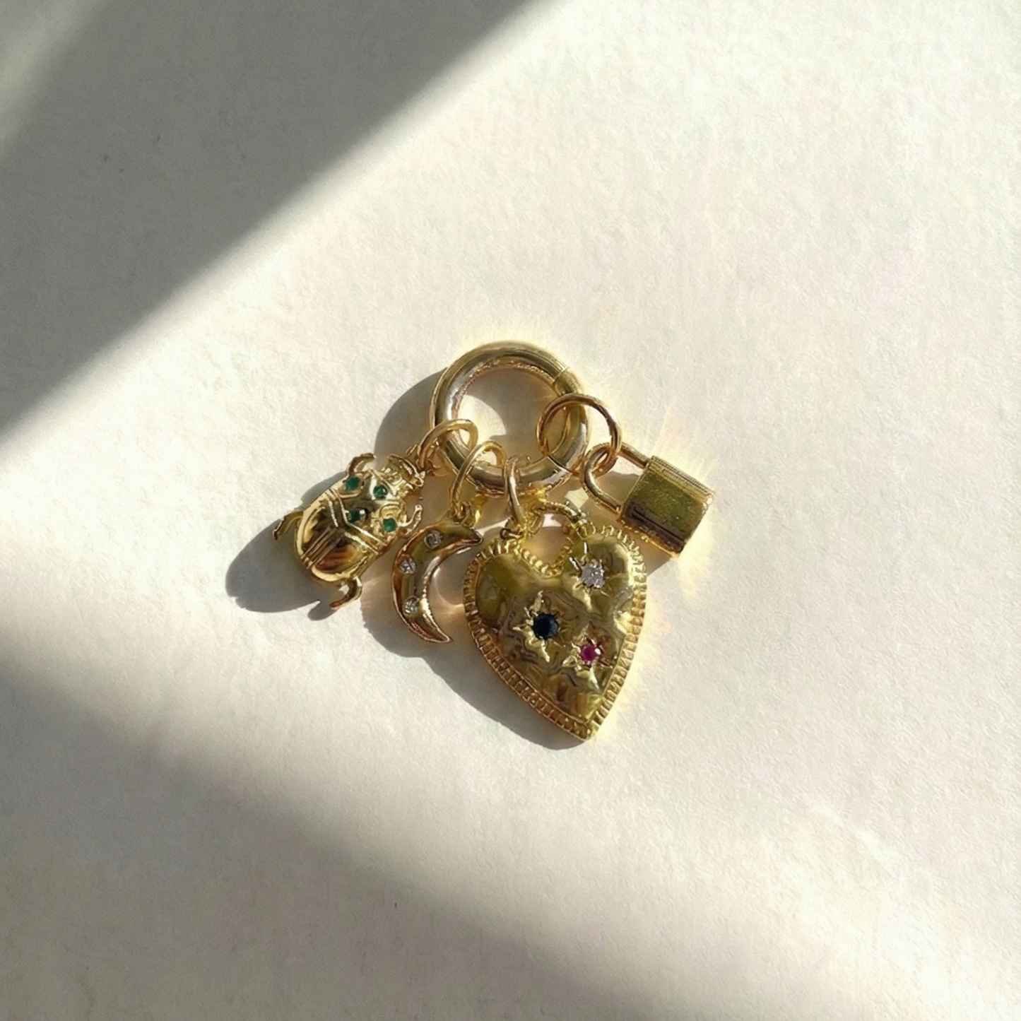 Gold charm with heart design and embedded stones on a white background